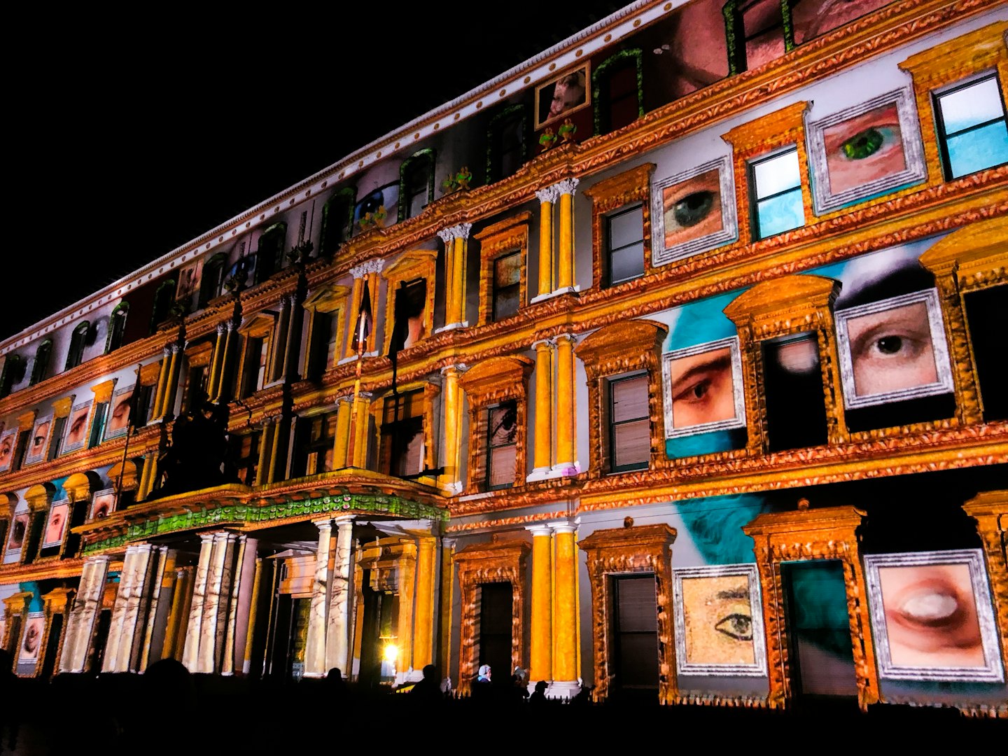 Building facade displaying human eyes and faces projected at night.