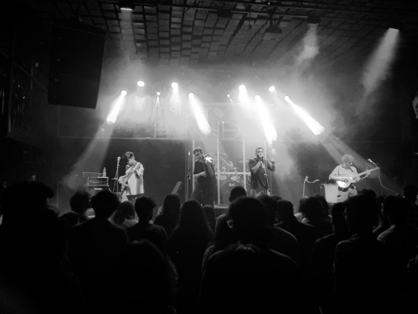 Musicians perform energetically on a concert stage with bright lights.